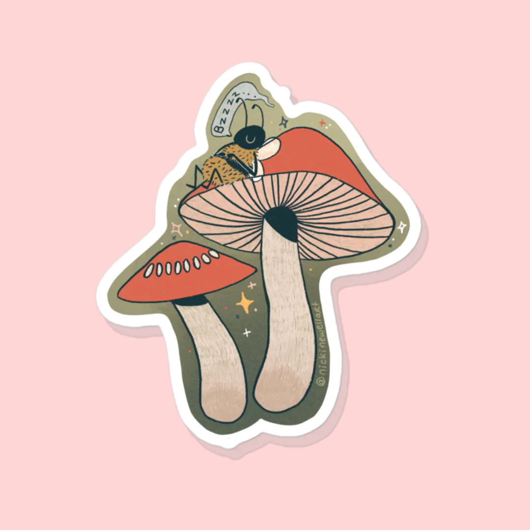 A picture of a sticker that has a little bee lounging on a red mushroom and snoozing.
